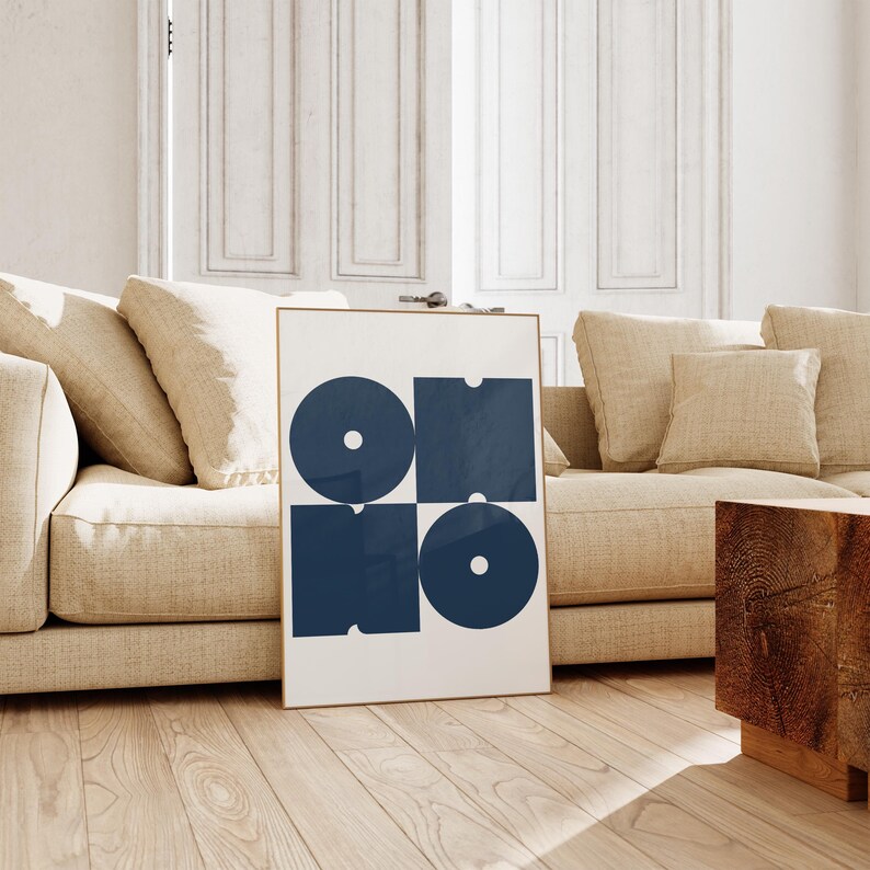 May include: A framed print with a white background and four navy blue geometric shapes. The shapes are arranged in a square pattern, with a circle in the top left corner, a square in the top right corner, a square in the bottom left corner, and a circle in the bottom right corner.