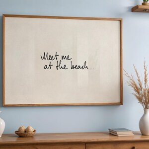 Puede incluir: Un estampado enmarcado con el texto "Meet me at the beach..." en escritura negra. El marco es de color marr&oacute;n c&aacute;lido, y el fondo es de color beige claro. El estampado se exhibe en un mueble de madera con objetos decorativos.