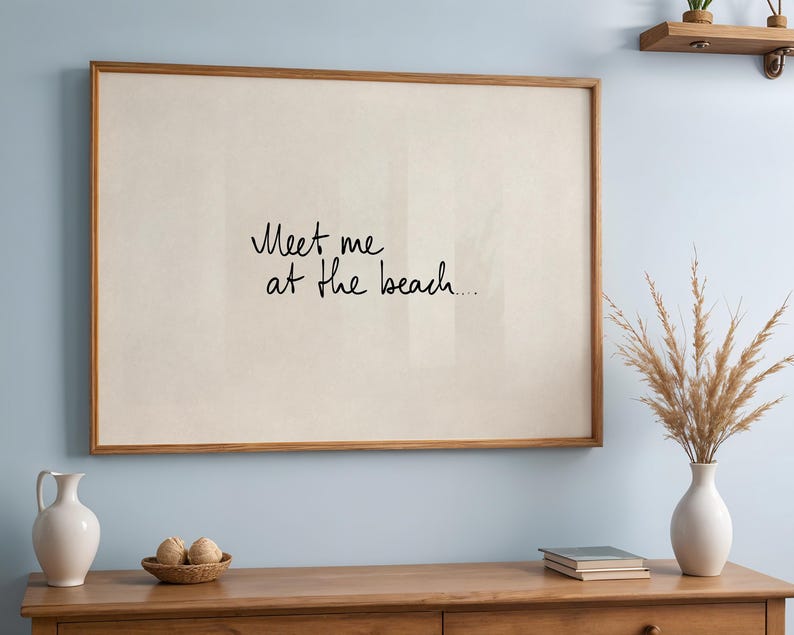 Puede incluir: Un estampado enmarcado con el texto "Meet me at the beach..." en escritura negra. El marco es de color marr&oacute;n c&aacute;lido, y el fondo es de color beige claro. El estampado se exhibe en un mueble de madera con objetos decorativos.