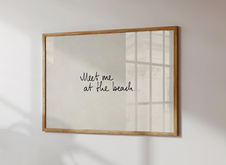 Puede incluir: Impresi&oacute;n enmarcada con el texto manuscrito "Meet me at the beach...". El marco es de madera clara y el fondo es de un beige neutro. La impresi&oacute;n se muestra en una pared blanca, con el reflejo de una ventana.