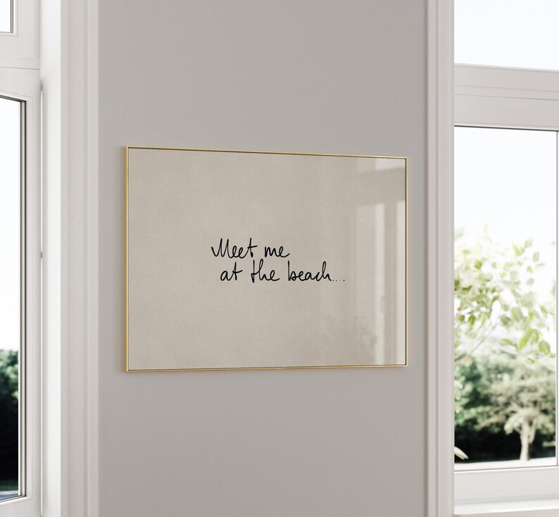 Puede incluir: Impresi&oacute;n rectangular enmarcada en dorado. La impresi&oacute;n presenta el texto manuscrito "Meet me at the beach..." en cursiva negra sobre un fondo beige. La obra enmarcada est&aacute; colgada en una pared gris claro.