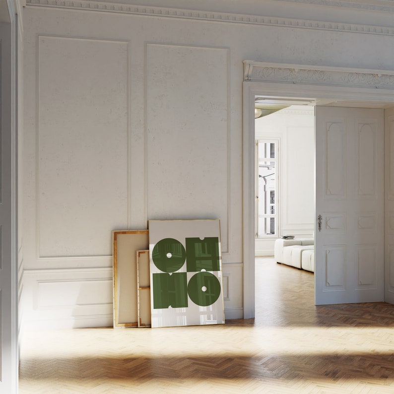 May include: A white room with a wooden floor. There are two framed pieces of art leaning against the wall. The art is a green and white abstract design with the word "OH NO" in the center.