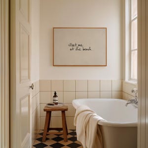 Puede incluir: Interior de ba&ntilde;o con un cuadro enmarcado con el texto "Meet me at the beach". Un taburete de madera sostiene una botella y una bandeja. Tambi&eacute;n se ven una ba&ntilde;era blanca y una ventana. El suelo tiene un patr&oacute;n de cuadros blancos y negros.
