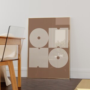 May include: A framed print with a geometric design featuring four white shapes on a brown background. The shapes are arranged in a grid pattern and resemble the letters "OHO".