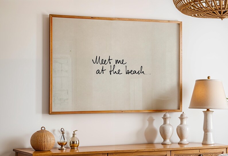 Puede incluir: Una impresi&oacute;n enmarcada con el texto escrito a mano "Meet me at the beach" en escritura negra. El marco es de madera marr&oacute;n claro. La impresi&oacute;n cuelga sobre un mueble de madera con objetos decorativos.