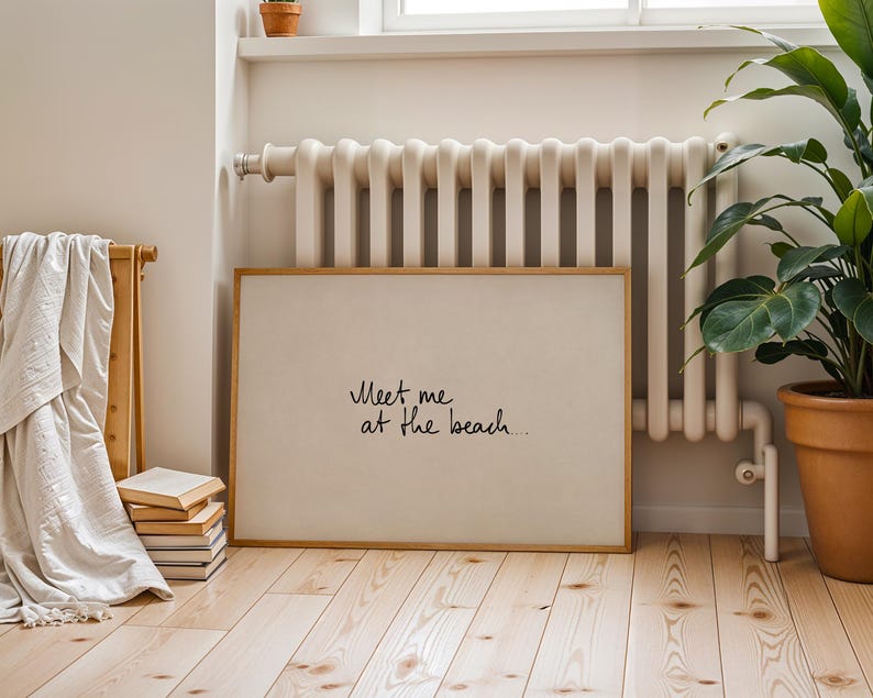 Puede incluir: Una impresi&oacute;n art&iacute;stica rectangular enmarcada con el texto "Meet me at the beach..." en escritura negra. La impresi&oacute;n tiene un fondo beige claro y un marco de madera natural. La impresi&oacute;n se exhibe en una habitaci&oacute;n con un radiador, una planta en maceta y una pila de libros.