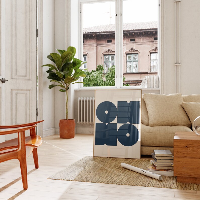 May include: A framed abstract art print with a geometric design of overlapping circles in shades of blue. The print is hanging on a white wall in a living room setting.