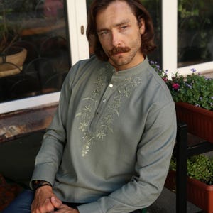 Puede incluir: Camisa de manga larga verde salvia con bordado floral alrededor del cuello y tapeta abotonada. La camisa tiene cuello mandar&iacute;n y se combina con vaqueros azules. La camisa est&aacute; hecha de un material suave y c&oacute;modo.