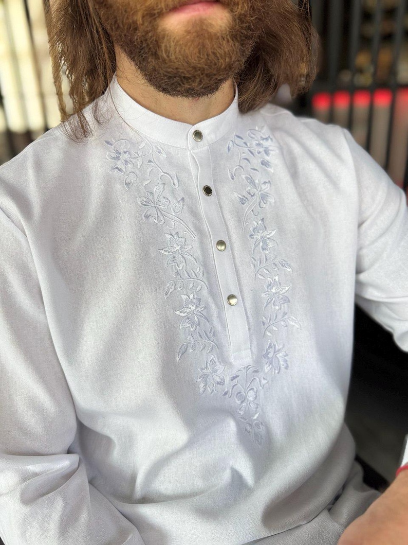 Puede incluir: Camisa blanca de manga larga con cuello mao y tapeta abotonada. La camisa presenta delicados bordados florales en la parte delantera. Hecha de una tela ligera.