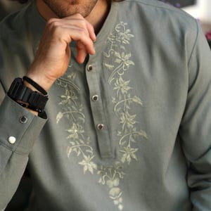 Puede incluir: Una camisa verde claro de manga larga con bordado floral en la parte delantera. La camisa tiene cuello mandar&iacute;n y pu&ntilde;os abotonados. El bordado es de un tono verde m&aacute;s claro. La camisa se usa con un reloj y una pulsera negros.