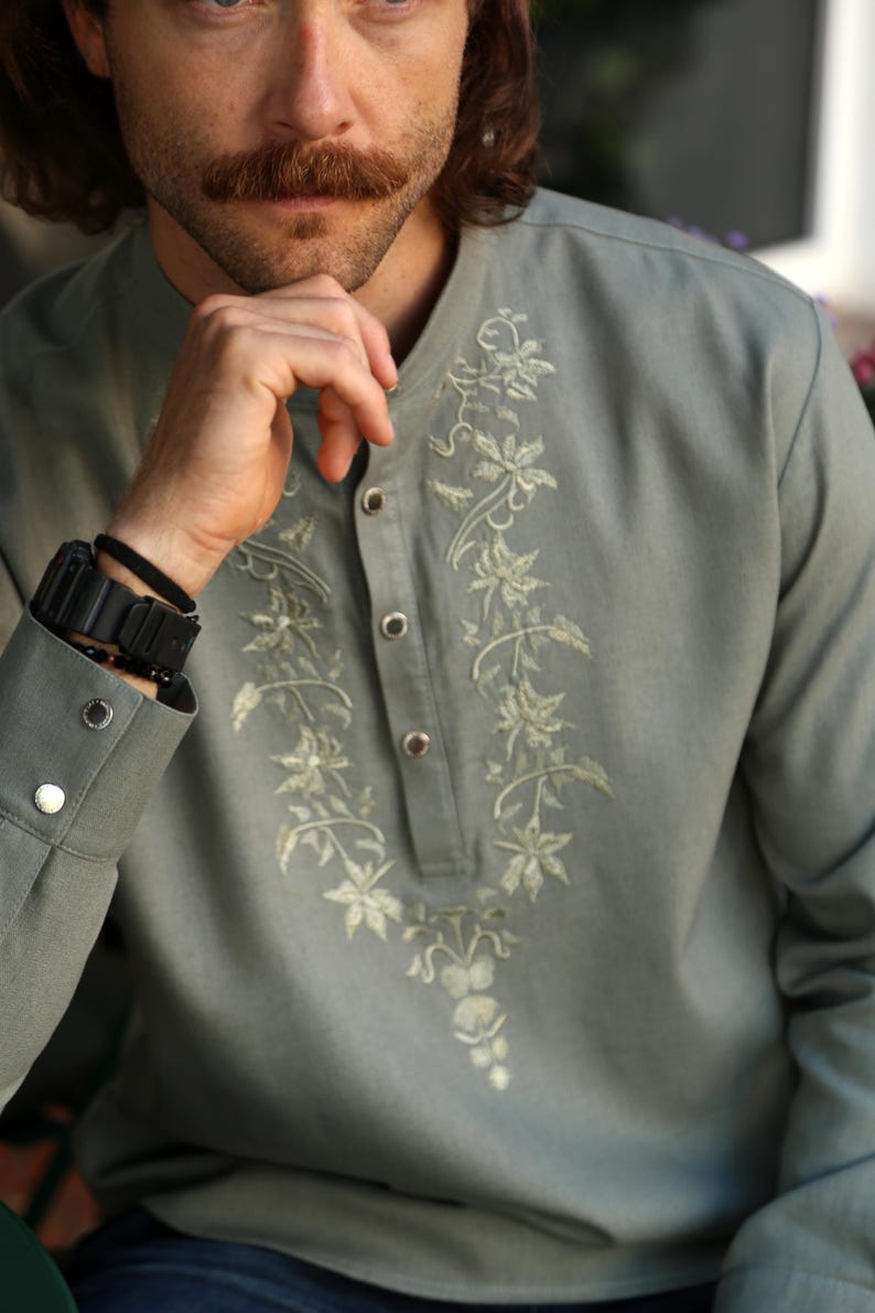 Puede incluir: Una camisa verde claro de manga larga con bordado floral en la parte delantera. La camisa tiene cuello mandar&iacute;n y pu&ntilde;os abotonados. El bordado es de un tono verde m&aacute;s claro. La camisa se usa con un reloj y una pulsera negros.