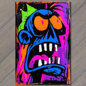 May include: A rectangular art print featuring a stylized blue creature head with large orange eyes, a wide open mouth with white teeth, and a pink tongue. The background consists of vibrant neon green, pink, and purple paint splatters and drips.