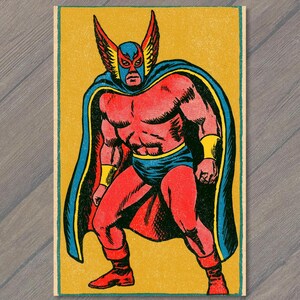 May include: A vintage-style comic book illustration of a masked wrestler standing in a dynamic pose. The figure wears a red bodysuit with a blue mask featuring winged ear details, a blue cape with yellow trim, and yellow wrist cuffs against a yellow background.