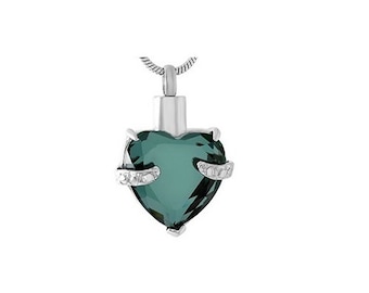 May include: A silver heart-shaped cremation pendant with a dark green crystal and small clear stones on the sides. The pendant is on a silver chain.