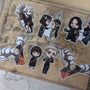 May include: A set of nine illustrated stickers featuring characters from popular fantasy television shows. The stickers are printed on white paper and feature a variety of characters, including elves, humans, and a creature with antlers. The stickers are perfect for adding a touch of fantasy to your laptop, water bottle, or planner.
