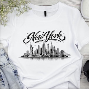 May include: White t-shirt with a black and white illustration of the New York City skyline, including the Statue of Liberty, skyscrapers, and the Brooklyn Bridge. The words "New York" are written in a decorative font above the skyline.