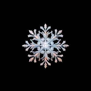 Puede incluir: Adorno de copo de nieve detallado con una combinación de colores azul claro y melocotón. El copo de nieve tiene un diseño intrincado y simétrico con bordes delicados y puntiagudos. El adorno está sobre un fondo negro.