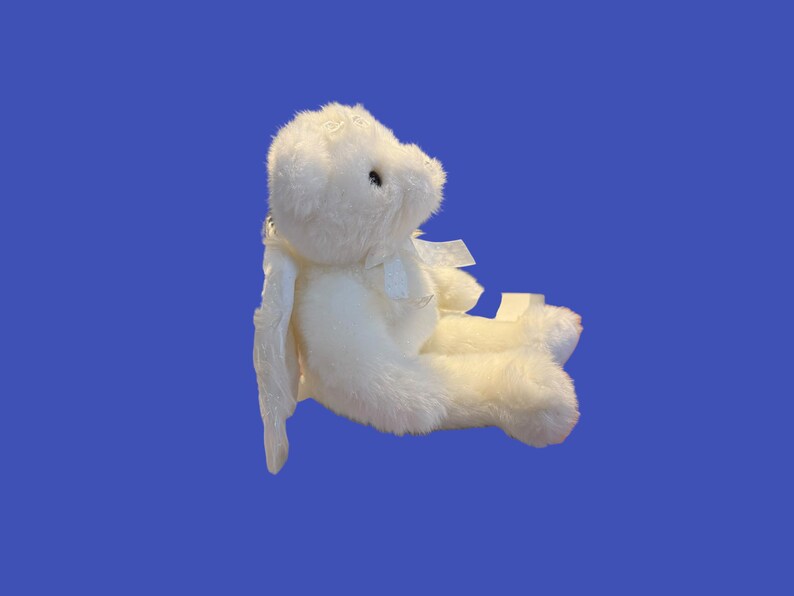 May include: A white plush bunny toy with long ears and a small bow. The bunny is sitting down, with its legs extended. The toy is made of soft, fluffy material and has black eyes.
