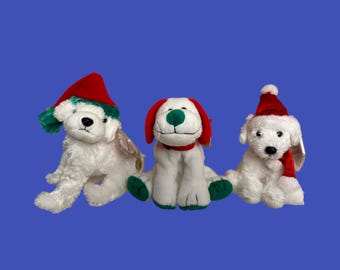 May include: Three white plush toy dogs wearing red and green Santa hats. The dogs are sitting on a blue background.