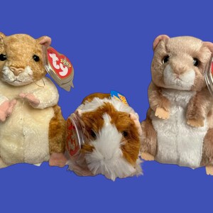 Peut inclure: Trois hamsters en peluche avec une fourrure brune et un ventre blanc. Chaque hamster a une étiquette Ty rouge et blanche attachée à lui. Les étiquettes portent le logo Ty et le mot "Ty" dessus.
