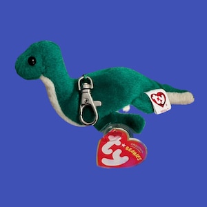 May include: Green plush dinosaur keychain with a silver clip and a red Ty Beanie Babies tag. The tag says "Original Beanie Babies".