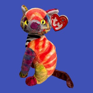 May include: A colorful, multi-patterned cat plush toy with a Ty Beanie Baby tag. The cat is sitting with its tail curled around its body. The plush toy is made of soft, fuzzy fabric and has a bright, cheerful expression.