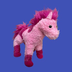 May include: A pink plush toy horse with a pink mane and tail. The horse has black eyes and a pink nose.