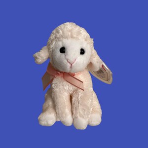 Könnte beinhalten: Ein weißes Plüschlamm mit einem rosa Band um den Hals. Das Lamm sitzt auf einem blauen Hintergrund.