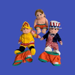May include: Three Beanie Baby dolls on a blue background. One doll is dressed as a firefighter in yellow and red. Another is dressed as Uncle Sam in red, white, and blue. The third doll is wearing orange shorts.
