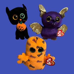 May include: Three Halloween-themed plush toys: a black cat holding a pumpkin, a purple bat with gold wings, and an orange ghost with the word "Boo" repeated on its body.