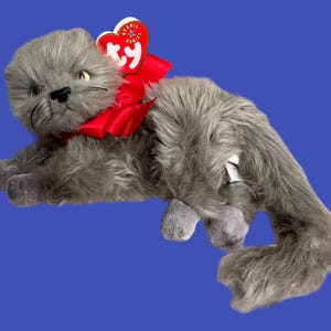 May include: Gray plush cat toy with a red bow and a Ty Beanie Babies tag. The cat has a white patch on its back.