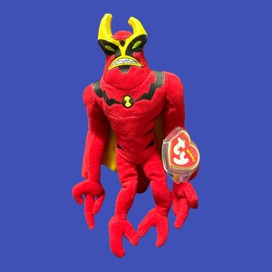 K&ouml;nnte beinhalten: Rotes und gelbes Pl&uuml;schtier eines Monsters mit H&ouml;rnern und einem Ty Beanie Babies-Etikett.
