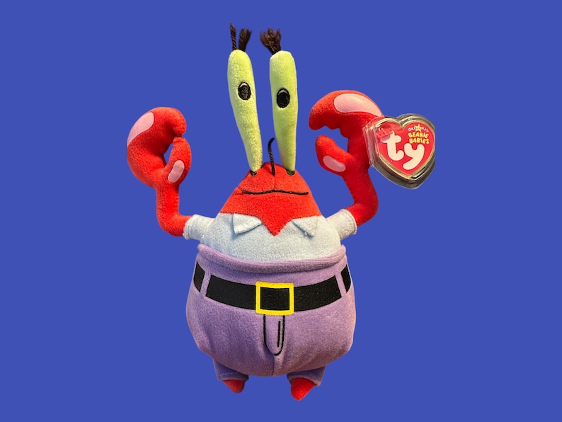 May include: A red and purple plush toy crab wearing a blue shirt and a black belt. The crab has green eyes and a red heart-shaped tag that says "Beanie Babies" and "Ty".