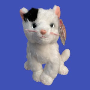 May include: White and black plush cat with pink nose and whiskers. The cat has a black patch on its forehead and is sitting with its tail curled around its legs. The cat has a Ty Beanie Baby tag attached to its ear.