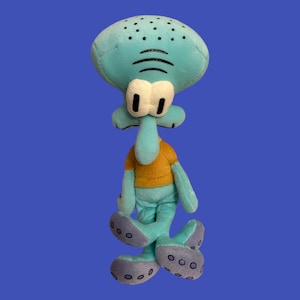 May include: A blue plush toy of Squidward Tentacles from the cartoon Spongebob Squarepants. He is wearing a yellow shirt and has a sad expression on his face.