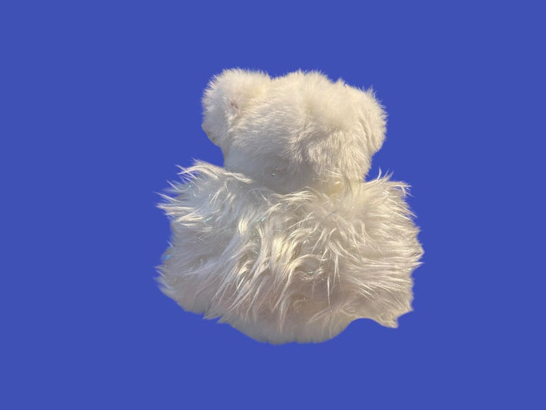 May include: A white, fluffy stuffed animal, possibly a bear, against a blue background. The toy has a shaggy texture and a soft appearance. The image is well-lit, highlighting the plush material.