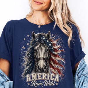 Peut inclure: Un t-shirt bleu marine à manches courtes orné d'un graphique représentant un cheval dont la crinière arbore les motifs du drapeau américain. Le design inclut des étoiles et le texte "AMERICA Runs Wild" en lettres blanches usées.