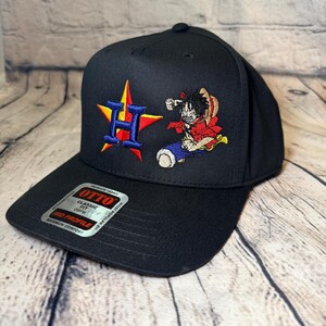 Op de afbeelding: Een zwarte honkbalpet met een geborduurde blauwe letter H over een rode en gele ster aan de linkerkant en een kleurrijk anime-personage met een strooien hoed aan de rechterkant. Een zilveren sticker op de klep vermeldt OTTO CLASSIC FIT OSFM MID PROFILE.