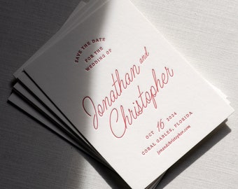 May include: A stack of off-white save the date cards with red text. The cards read: Save the date for the wedding of Jonathan and Christopher, Oct 16 2024, Coral Gables, Florida, and the website address jonandchristopher.com.