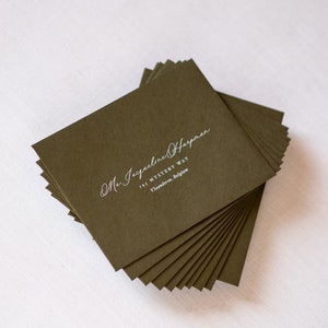 May include: A stack of dark green envelopes with white calligraphy that reads "Mr. Jacqueline Harman 193 Mystery Way Vlaanderen, Belgium"