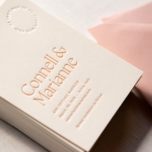 May include: White wedding invitation cards with gold lettering announcing the marriage of Connell & Marianne. The text reads "Are getting married March 20, 2025 Ischia, Italy cannellandmarianna.com Formal invitation to follow"