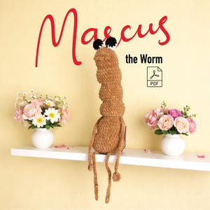 Puede incluir: Un juguete de peluche con forma de gusano marrón con ojos negros y blancos, sentado en un estante blanco. El texto "Marcus the Worm" está escrito en rojo encima del gusano. Un icono PDF es visible.