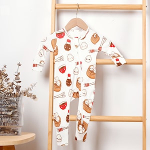 May include: White baby onesie with a zipper closure and a print of cartoon dumplings, chopsticks, and soy sauce.