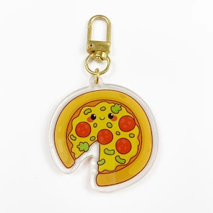 Puede incluir: Un llavero de rebanada de pizza de acrílico transparente con un cierre dorado. La pizza tiene una cara sonriente, pepperoni rojo, pimientos verdes y una rebanada que falta. La corteza es amarilla y los ingredientes son coloridos.