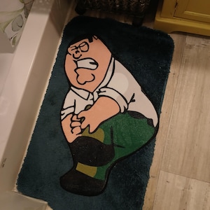 Peut inclure: Un tapis de bain bleu canard repr&eacute;sentant un personnage de dessin anim&eacute; portant une chemise blanche, un pantalon vert et des chaussures noires. Le personnage a une expression surprise. Le tapis est rectangulaire et pos&eacute; sur le sol d'une salle de bain.