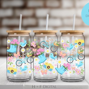 Puede incluir: Tres vasos de vidrio con tapas de bambú y pajitas. Cada vaso está decorado con un diseño de temática primaveral con pájaros azules, bicicletas, flores, mariposas y cámaras. El texto "DIGITAL DOWNLOAD" está en un círculo azul.