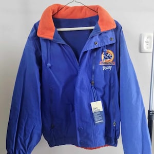 May include: Blue and orange fleece-lined jacket with a Tide Racing Downy logo. The jacket has a zipper closure and a drawstring hood.