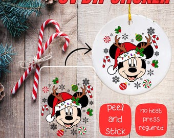 May include: A Christmas-themed UV DTF sticker featuring Mickey Mouse wearing a Santa hat with reindeer antlers, surrounded by candy canes, snowflakes, and ornaments. The sticker is shown next to a ceramic ornament with the same design and two candy canes.