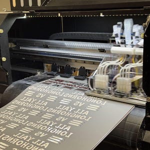 a large printer with a printed document or material resting on top of it. The printer appears to be in operation, as the document is visible on the surface.
