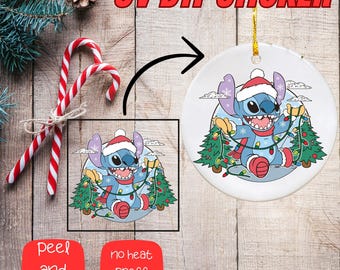 May include: A white ceramic Christmas ornament featuring a cartoon character wearing a Santa hat, scarf, and holding Christmas lights and trees. The image includes the text "UV DTF STICKER". Candy canes and a pinecone are also visible.